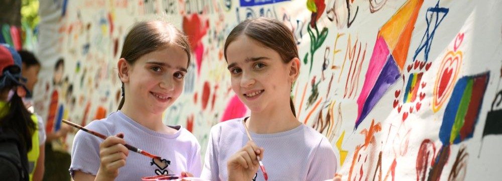 Two young girls holding paintbrushes in front of a mural.